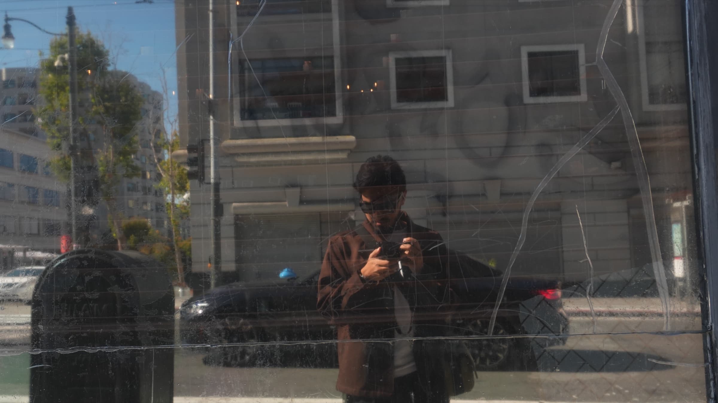 Self-portrait reflected in a cracked storefront window, camera in hand